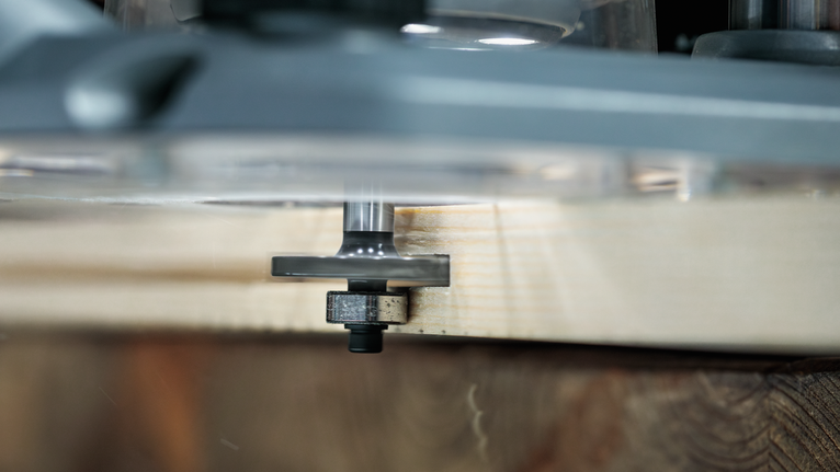 Wood router cutting a groove along the edge of a wooden board.