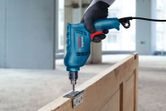 A person wearing safety equipment uses a power drill to install a hinge on a wooden door.