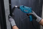 A person wearing safety equipment drills a hole into a metal surface.
