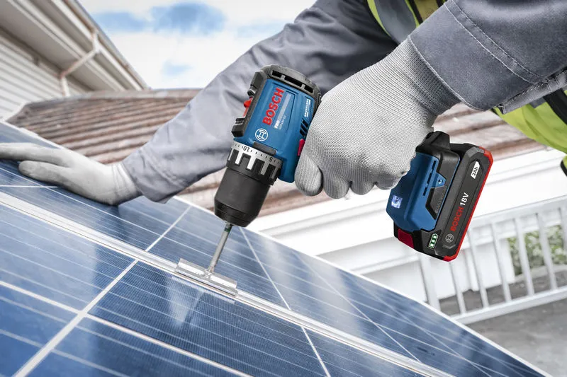 A person wearing safety equipment uses a cordless drill on a solar panel.
