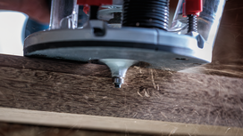 Wood router shaping the edge of a plank, creating wood shavings.