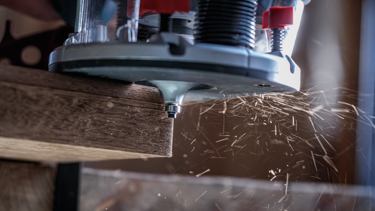 Wood router shaping the edge of a board, creating wood shavings.