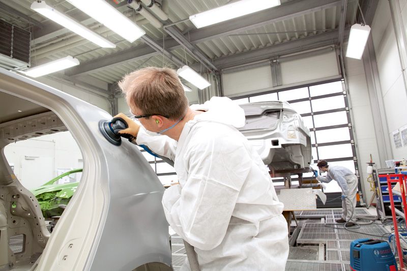 A person wearing safety equipment polishes a car body in a workshop.