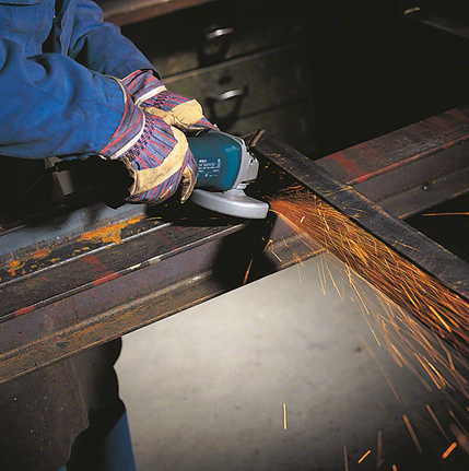 Person wearing safety equipment grinds a metal beam, producing bright sparks.