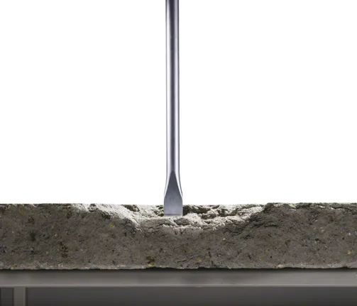Flat chisel bit breaking into a concrete slab.