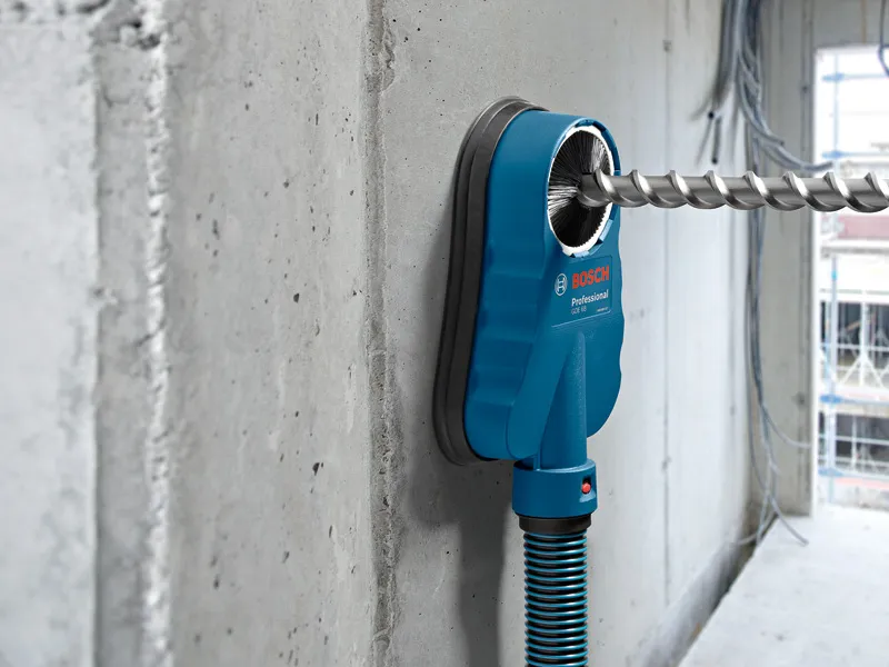 Drill dust extraction system attached to a concrete wall with an inserted drill bit.
