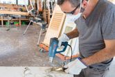 A person wearing safety equipment uses a heat gun to remove paint from a wooden surface.