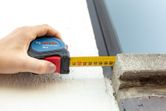 A person measures a wall edge with a tape measure.