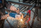 A person wearing safety equipment grinds metal with an angle grinder, producing sparks.