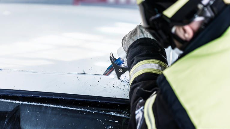 Person wearing safety equipment cuts vehicle windshield with a power tool.