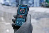 Person wearing safety equipment holds a laser measure displaying language options.