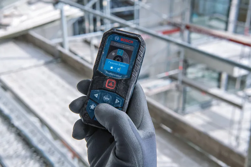 Person wearing safety equipment holds a laser measure at a construction site.