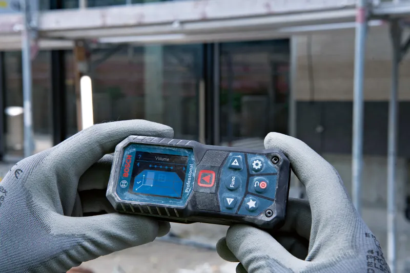 A person wearing safety equipment holds a laser measure at a construction site.