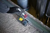 Person wearing safety equipment marking a metal channel with a laser measure beside them.