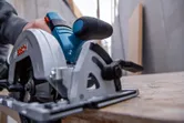 A person guides a circular saw along a wooden board in a workshop.