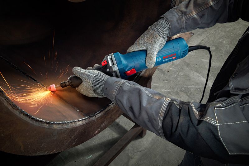 A person wearing safety equipment uses a straight grinder to grind metal, creating sparks.