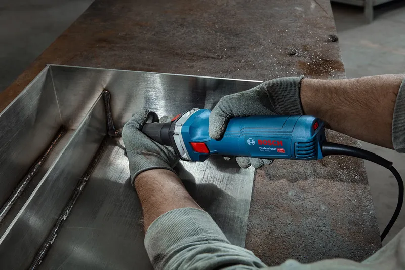 A person wearing safety equipment grinds a welded metal seam with a straight grinder.