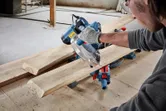 A person wearing safety equipment uses a circular saw to cut wooden planks.