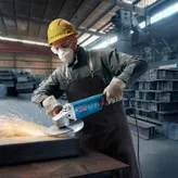 A person wearing safety equipment grinds metal with a large angle grinder, producing sparks.