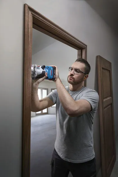A person wearing safety equipment uses a router to trim a wooden door frame.