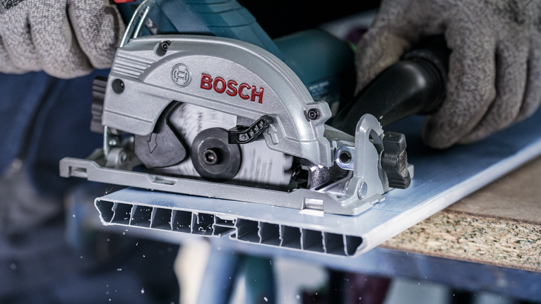 Person wearing safety equipment cuts a metal sheet with a circular saw.