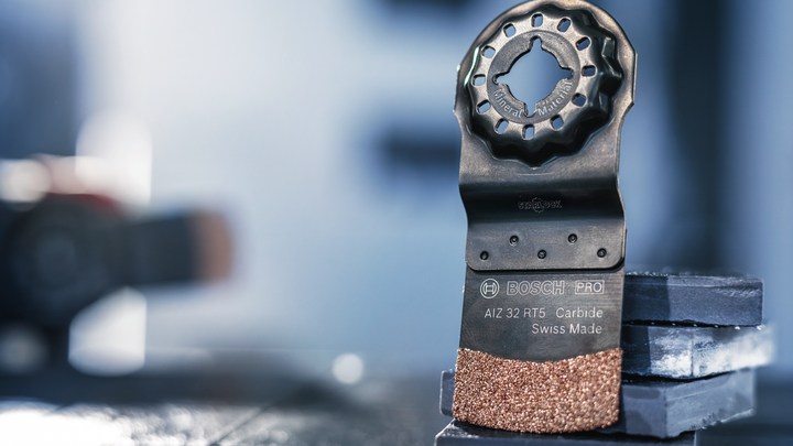 Oscillating multi-tool carbide blade standing upright on stacked tiles.