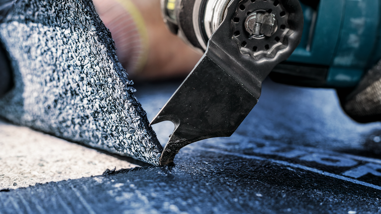 A person wearing safety equipment uses a power tool to cut flooring material.