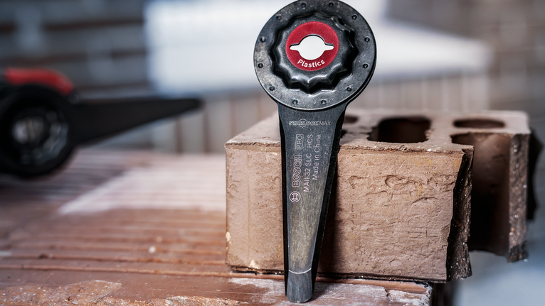 Oscillating tool accessory for cutting plastics resting on a concrete block.