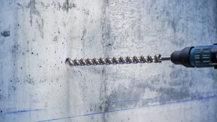 Rotary hammer with a long drill bit making a hole in a concrete wall.