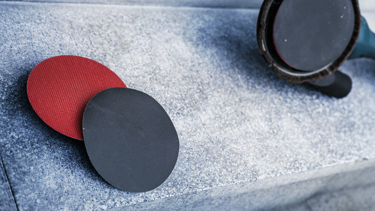 A polishing tool and sanding discs lie on a rough stone surface.