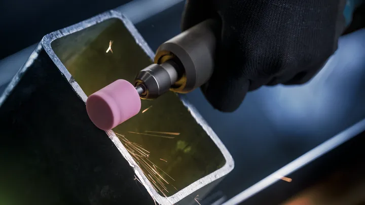 Person wearing safety equipment grinds the edge of a metal tube with a rotary tool.