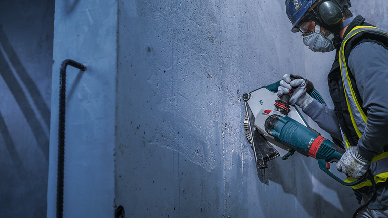 A person wearing safety equipment cuts into a concrete wall using a power tool.