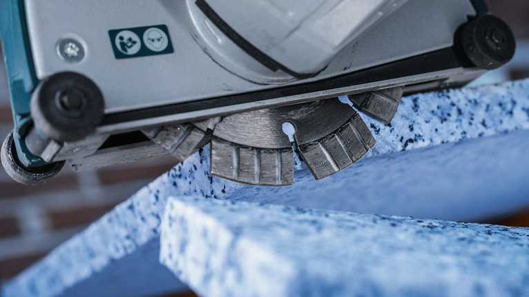Diamond cutting blade slices through a speckled blue stone slab.
