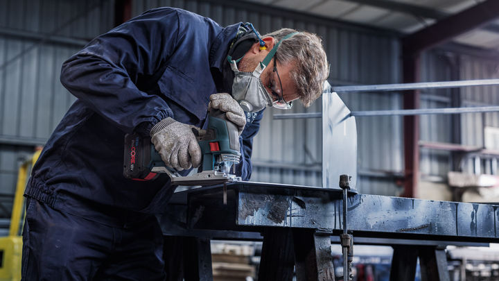 A person wearing safety equipment uses a power tool to cut metal in a workshop.