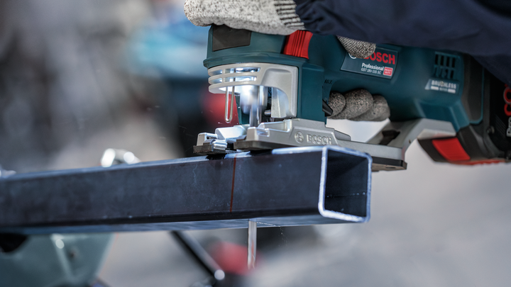 Person wearing safety equipment cuts a metal beam with a handheld power saw.