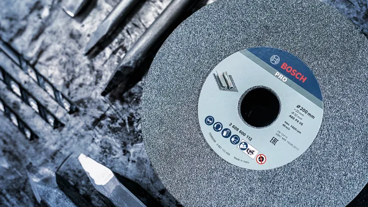 Large grinding wheel placed among several metal drill bits on a rough work surface.