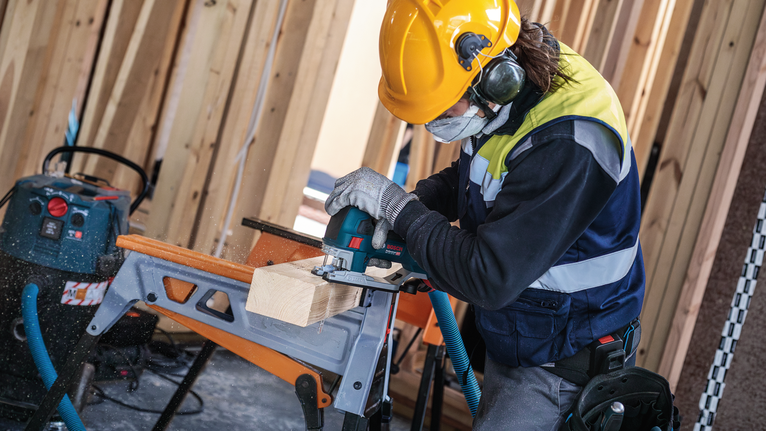 Person wearing safety equipment cuts a wooden beam with a power saw.