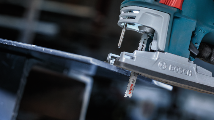 Jigsaw cutting through a metal sheet in a workshop.