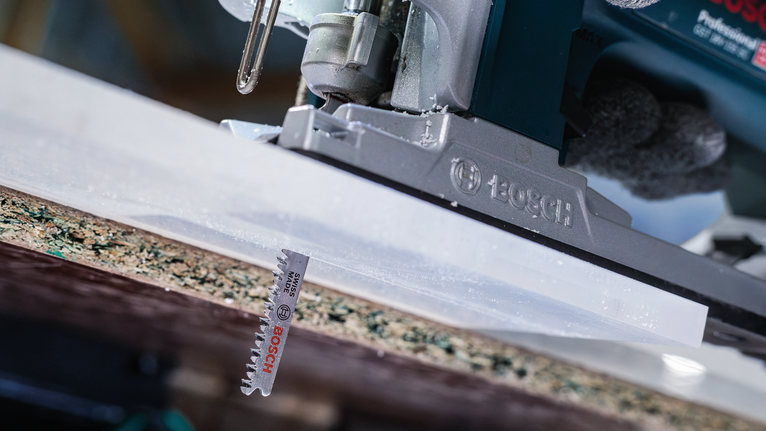Person wearing safety equipment cuts a board using a jigsaw.