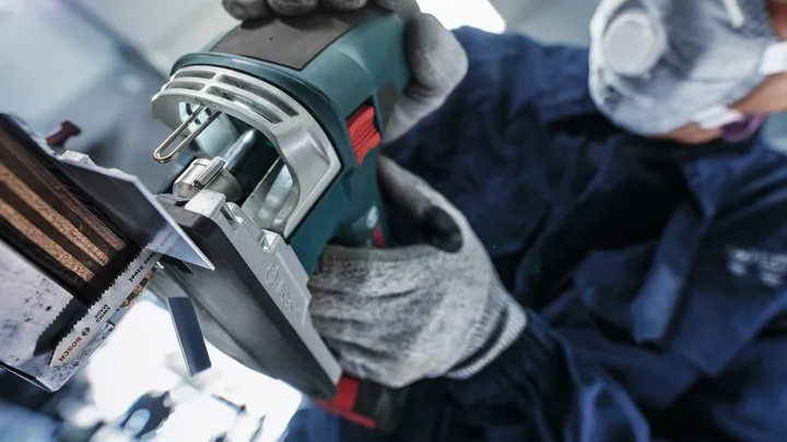 A person wearing safety equipment operates a power tool to cut a metal piece.