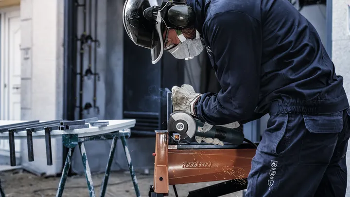 A person wearing safety equipment grinds metal, producing sparks.