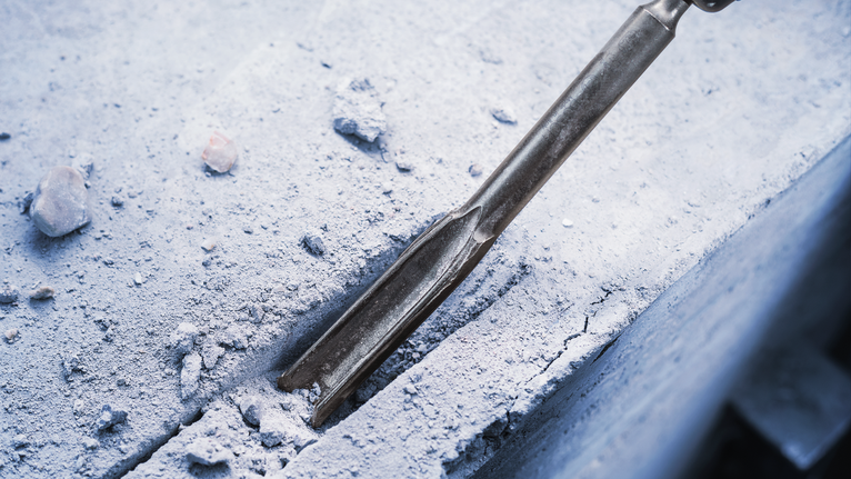 Chisel attachment breaking a straight groove into a concrete surface.