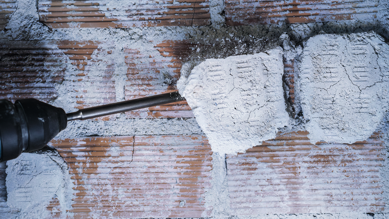 Rotary hammer breaking plaster off a brick wall.