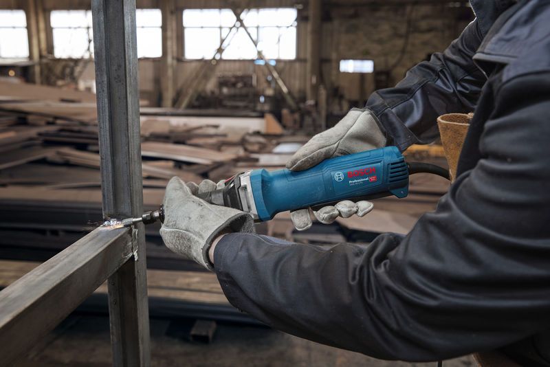 A person wearing safety equipment grinds a metal frame with a straight grinder.