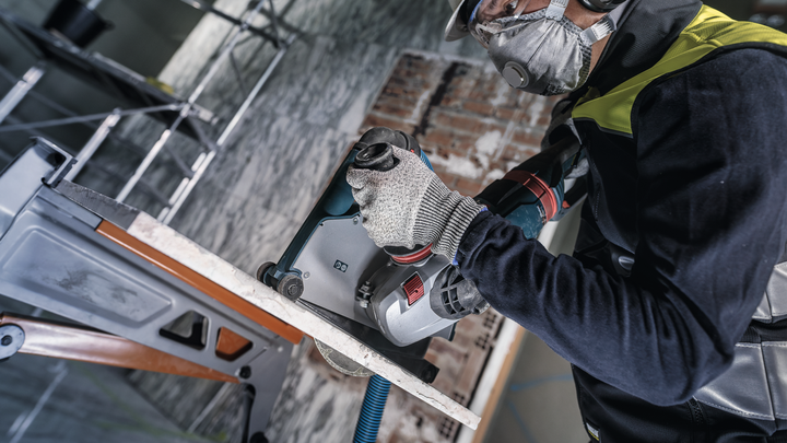 Person wearing safety equipment drills into a concrete wall with a power tool.