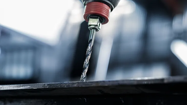 Drill making a hole through a metal sheet.