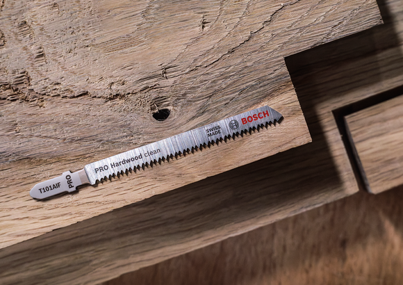 Jigsaw blade placed on a wooden surface with a cutout section.