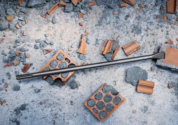 Chisel bit lying on broken bricks and concrete debris.