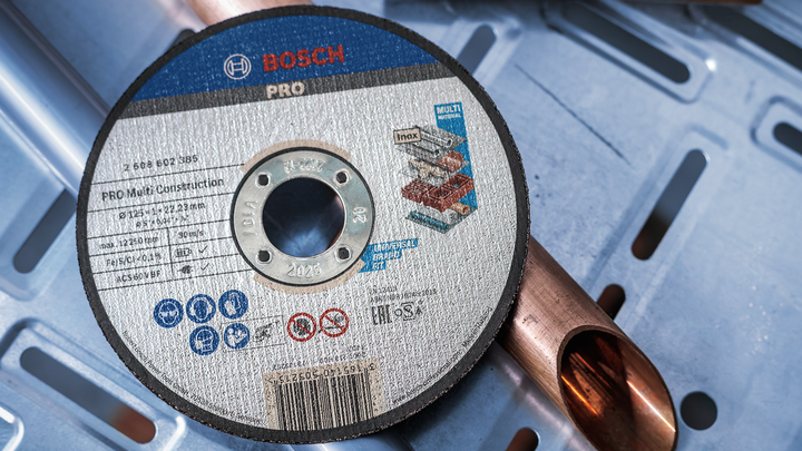 Cutting disc resting on a copper pipe on a blue perforated metal surface.