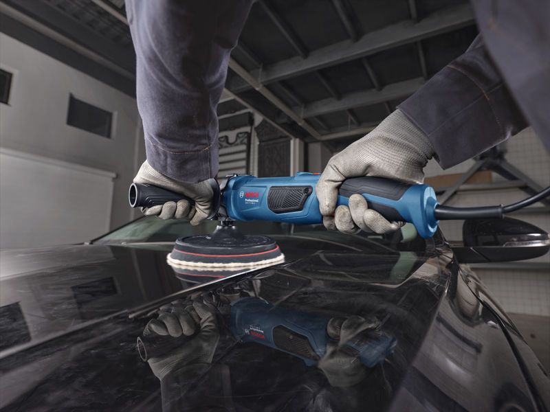 A person wearing safety equipment polishes a car hood with a blue polisher.